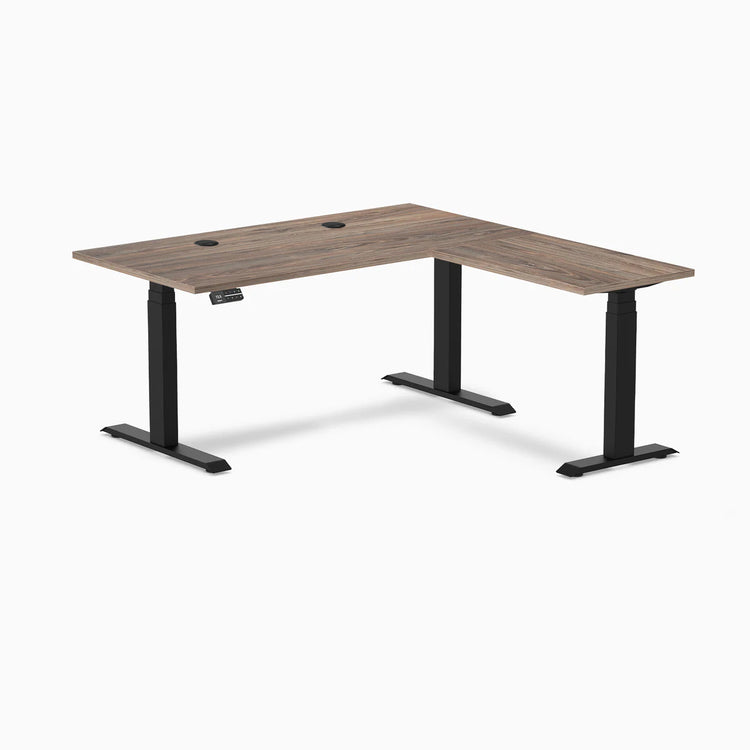 Natural Walnut L-shape laminate sit-stand desk with matte black frame and grommets.